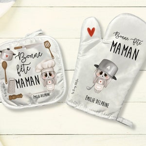 May include: A set of two white oven mitts with a bunny rabbit design. The mitts feature the text "Bonne fete Maman" and the name "Emilie Delphine".