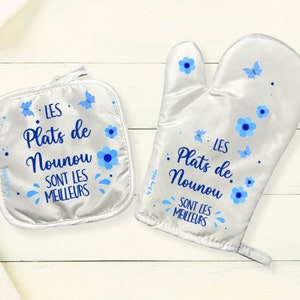 May include: A set of two white oven mitts with blue floral and butterfly designs. The mitts have the text "LES Plats de Nounou SONT LES MEILLEURS" printed on them.