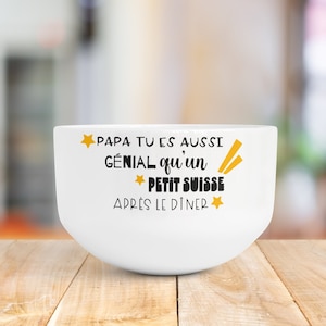 Peut inclure: Un bol en céramique blanc avec le texte noir "PAPA TU ES AUSSI GÉNIAL qu'un PETIT SUISSE APRÈS LE DÎNER" imprimé sur la face avant, accompagné de petites étoiles jaunes et de deux lignes diagonales jaunes décoratives.