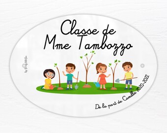 May include: Oval-shaped classroom door sign with the text "Classe de Mme Tambozzo" and a small illustration of children planting trees. The sign also includes the text "De la part de Camille 2020-2022".