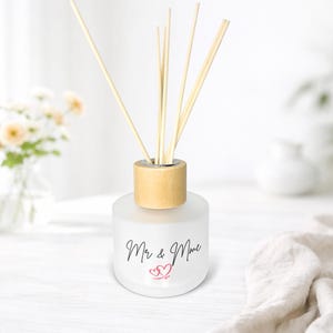 May include: A frosted glass diffuser bottle with a wooden cap and reeds. The bottle is decorated with the words "Mr & Mme" and two red hearts. The background is white with a soft focus.