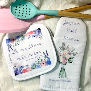 May include: Two white oven mitts with floral designs. One mitt has the text "La meilleure cuisinière de la part d'Olivier" and the other has the text "Joyeux Noël Mamie de la part d'Olivier".