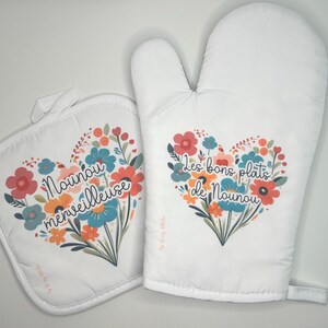 May include: A set of two white oven mitts with floral designs and French text. The smaller mitt has the text "Nounou merveilleuse" and the larger mitt has the text "Les bons plats de Nounou".
