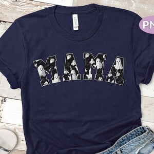 May include: Navy blue t-shirt with the word "MAMA" in white block letters. The letters are filled with a pattern of white ghosts on a black background. The shirt has rolled-up sleeves.
