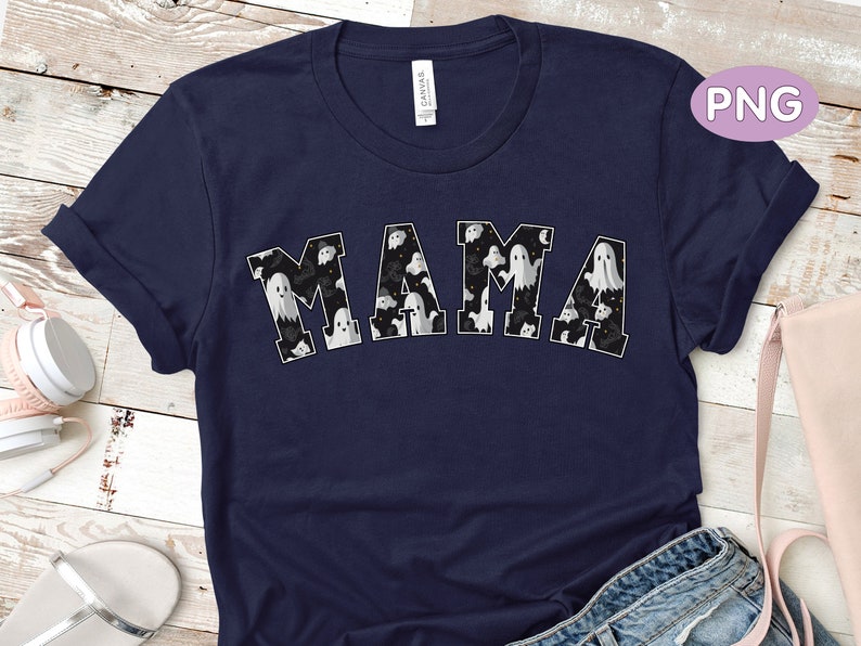 May include: Navy blue t-shirt with the word "MAMA" in white block letters. The letters are filled with a pattern of white ghosts on a black background. The shirt has rolled-up sleeves.