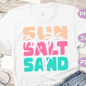 May include: White t-shirt with the words "SUN SALT SAND" in peach, pink, and teal block letters. Palm tree silhouettes are incorporated into the word "SUN". The shirt is a casual summer design.