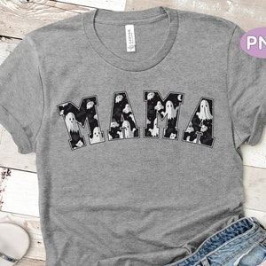 May include: A gray t-shirt with the word "MAMA" in a black and white ghost-themed design. The letters are filled with various ghost illustrations. The shirt is made of a soft material and has rolled-up sleeves.