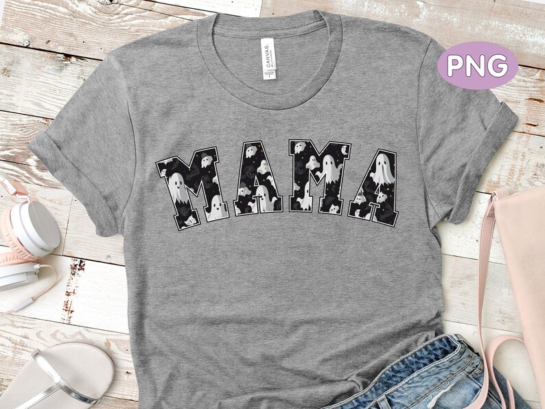 May include: A gray t-shirt with the word "MAMA" in a black and white ghost-themed design. The letters are filled with various ghost illustrations. The shirt is made of a soft material and has rolled-up sleeves.