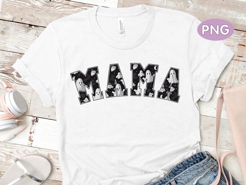 May include: White t-shirt with the word "MAMA" in black block letters. The letters are filled with a pattern of ghosts and bats. The shirt has short sleeves and a crew neck.
