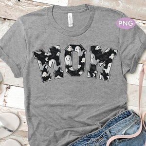 May include: A grey t-shirt with the word "MOM" printed in black outlined letters. The letters are filled with a pattern of white ghosts on a black background.