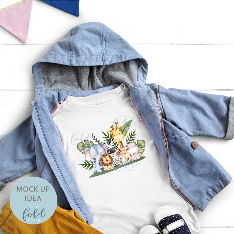 May include: White t-shirt with a graphic of a group of jungle animals including a giraffe, zebra, lion, elephant, and a monkey. The text "On the Fold Designs" is printed below the animals.
