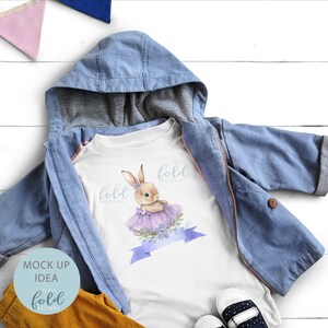Peut inclure: T-shirt blanc pour enfant avec une illustration aquarelle d'un lapin brun portant un tutu violet et un ruban bleu avec le texte "On the Fold Designs".