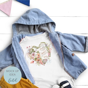 May include: White t-shirt with a floral heart design and the text "Happy Mother's Day". The shirt is on a white wooden surface with a blue jacket and yellow pants.