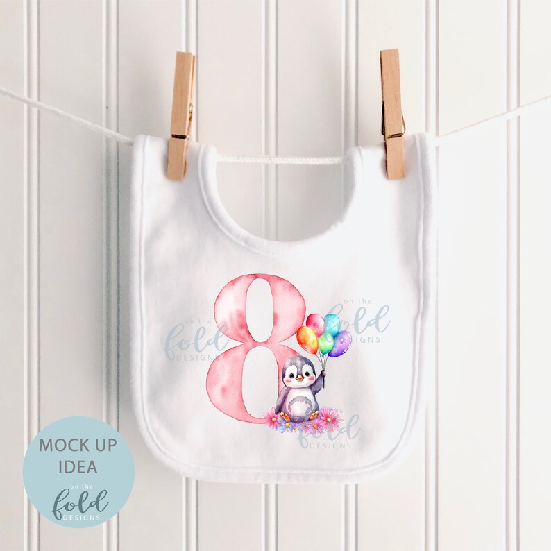 May include: White bib with a pink number eight and a penguin holding rainbow balloons. The text "On the Fold Designs" is on the bib.