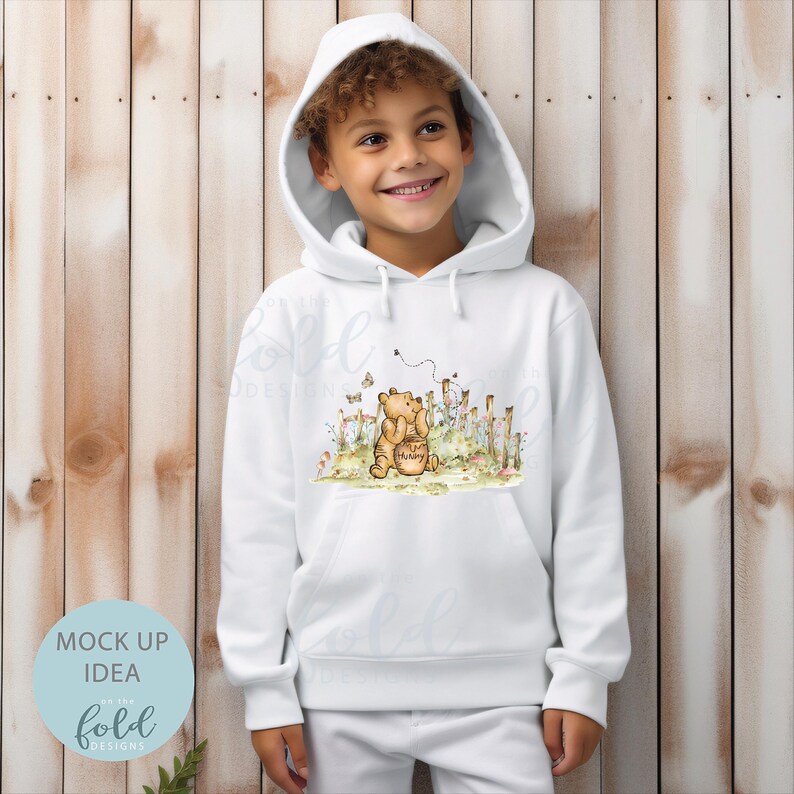 May include: White hooded sweatshirt featuring an illustration of Winnie the Pooh and Piglet. The illustration depicts Winnie the Pooh holding a honey pot with Piglet standing behind him. The illustration is surrounded by flowers and a fence.
