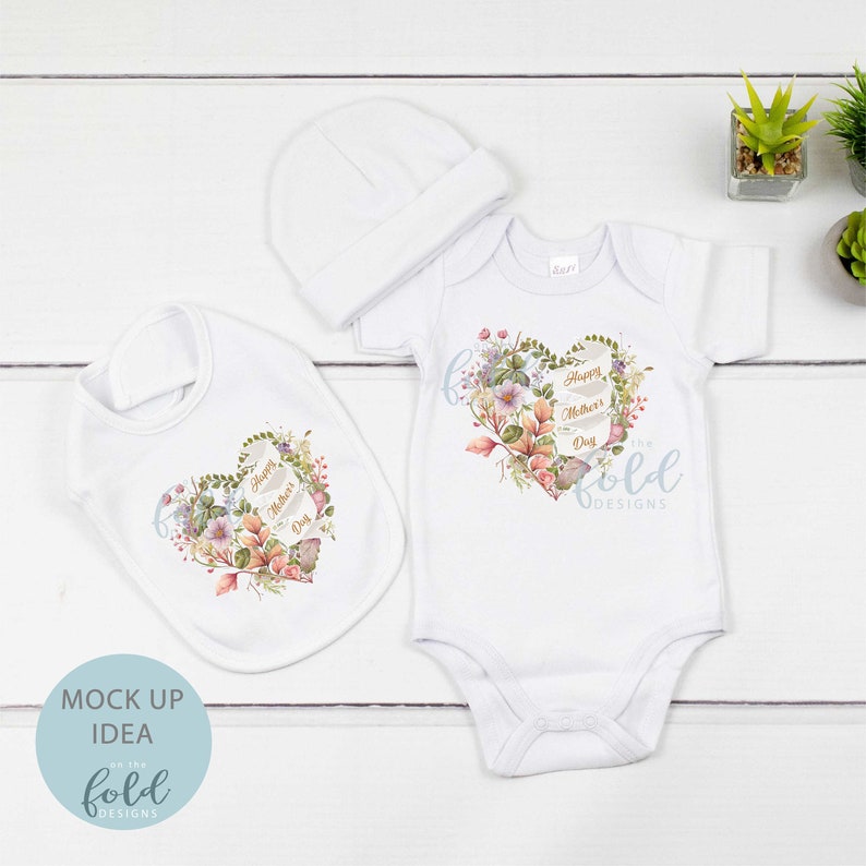 May include: A white baby bodysuit, bib, and hat with a floral heart design and the text "Happy Mother's Day".