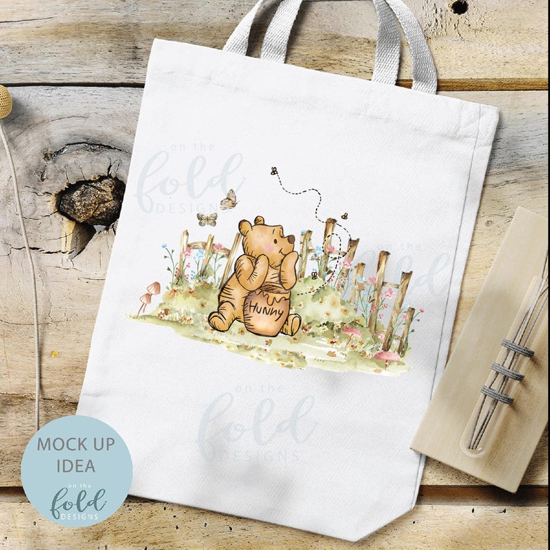 May include: White tote bag featuring a watercolour illustration of Winnie the Pooh holding a honey pot. The illustration is surrounded by flowers and a fence. The text "Hunny" is on the honey pot.