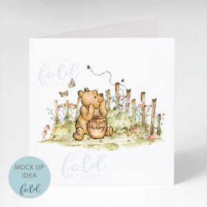 May include: A watercolour illustration of Winnie the Pooh holding a honey pot with the text "Hunny" on it. He is standing in a field of flowers with a wooden fence behind him. The text "On the Fold Designs" is at the top and bottom of the image.