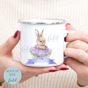 Peut inclure: Mug en &eacute;mail blanc avec un motif de lapin brun portant un tutu violet et un ruban bleu avec le texte "on the fold designs".