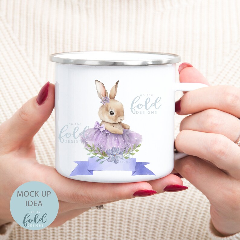 Peut inclure: Mug en &eacute;mail blanc avec un motif de lapin brun portant un tutu violet et un ruban bleu avec le texte "on the fold designs".