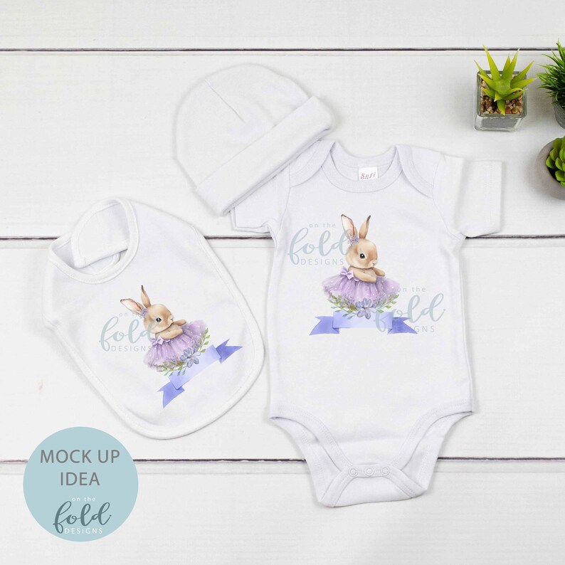 Peut inclure: Un body b&eacute;b&eacute; blanc et une bavette avec une illustration de lapin violet et blanc. Le lapin porte un tutu violet et tient une fleur. Le texte "on the fold designs" est imprim&eacute; sur le body et la bavette.