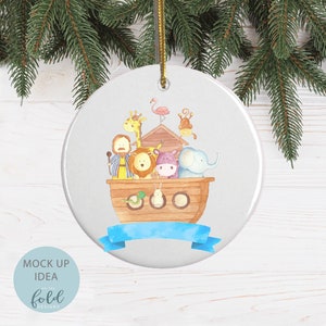 May include: A round white Christmas ornament with a watercolor illustration of Noah's Ark. The ark is filled with pairs of animals, including a giraffe, lion, hippo, and elephant. A blue ribbon is at the bottom. The ornament is hanging from a gold string.