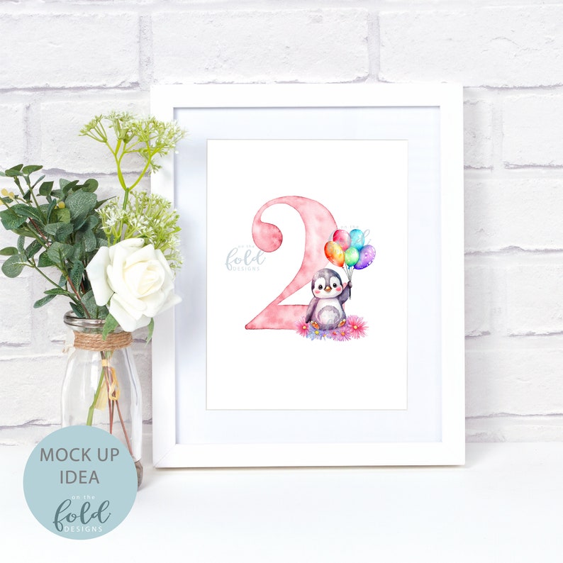 May include: A white frame with a pink watercolor illustration of the number two. A penguin with black and white feathers is holding a bunch of colorful balloons. The text "fold designs" is in the bottom left corner of the image.