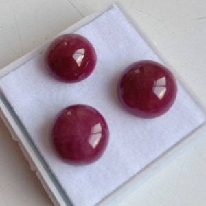 May include: Three round, cabochon-cut, deep red gemstones in a white, felt-lined box.