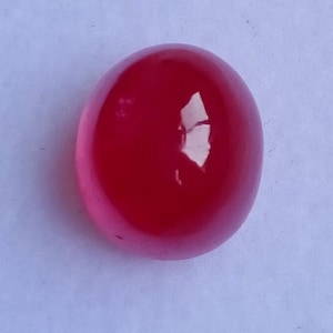 May include: A smooth, round, pink cabochon gemstone. The stone is polished and has a glossy finish.