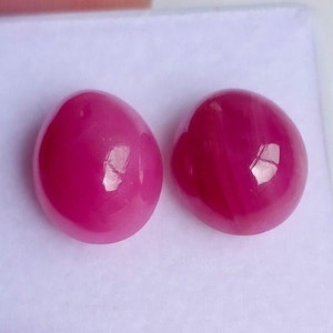 May include: Two round, pink cabochon gemstones on a white background.