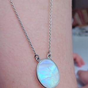 May include: A silver chain necklace with a large oval-shaped iridescent gemstone pendant.