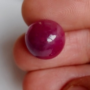 Op de afbeelding: Een ronde, cabochon geslepen robijn met een dieprode kleur. De edelsteen is gepolijst en heeft een glanzende afwerking.