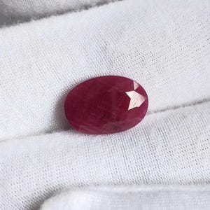 Peut inclure: Une pierre précieuse rubis de forme ovale à facettes, dotée d'une couleur rouge profond et d'une surface polie. La pierre présente une taille à facettes claire qui reflète la lumière sur toute sa surface, révélant une teinte rouge vive et saturée.
