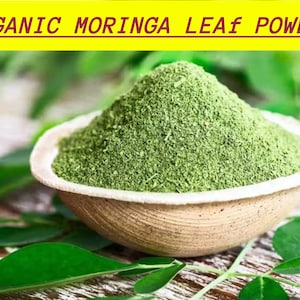 May include: A bowl of green moringa leaf powder, with the text "ORGANIC MORINGA LEAF POWDER" above. The bowl is light brown and rests on a surface with green leaves. The image is a close-up shot.