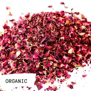 May include: A pile of dried rose petals, labelled "ORGANIC", on a white background. The petals are a deep pink colour and have a slightly textured surface.