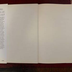May include: An open book titled "Art and Symbols of the Occult" with blank pages. The left page features text describing the book's content. The book is on a dark red surface.