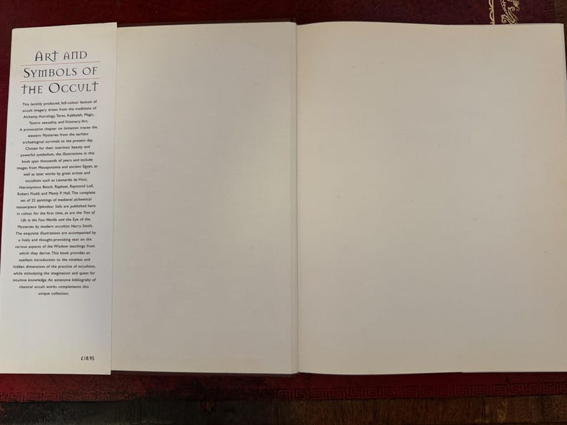 May include: An open book titled "Art and Symbols of the Occult" with blank pages. The left page features text describing the book's content. The book is on a dark red surface.