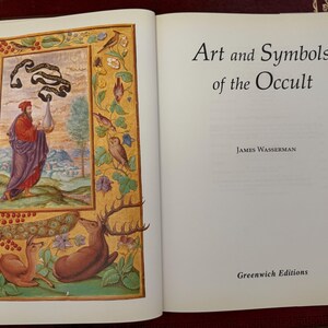 May include: An open book with the title "Art and Symbols of the Occult" by James Wasserman. The left page features a colorful illustration with a figure in red and purple robes, surrounded by birds, deer, and floral elements.