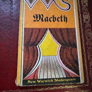 Peut inclure: Un livre de poche intitulé Macbeth de la série New Warwick Shakespeare. La couverture présente un fond jaune avec une lettre S stylisée, une illustration graphique d'une scène avec des rideaux rouge foncé et un plancher en noir et blanc.
