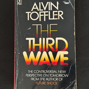 May include: A well-worn copy of Alvin Toffler's book, "The Third Wave". The cover is black with white and yellow lettering, and the title is in a gradient of yellow to red. The book is described as a controversial new perspective on tomorrow.