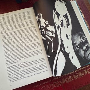 May include: Open book with black and white illustrations of figures and text. The book is open to a page with a large illustration of a figure with a dark background. The text is in English.