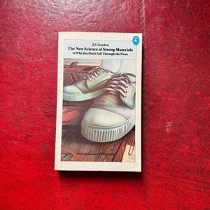 Könnte beinhalten: Ein Taschenbuch mit dem Titel The New Science of Strong Materials or Why You Don't Fall Through the Floor von J.E. Gordon. Das Cover zeigt eine Illustration eines Paares weißer Turnschuhe auf einem Holzboden mit einer kleinen Maus.