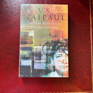 May include: A hardcover book titled Letters Between a Father and Son by V.S. Naipaul. The cover features a collage with a bicycle, a typewriter, a building, and a portrait of a person, all set against a warm, multi-colored background.