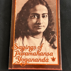 Może przedstawiać: Prostokątna okładka książki z portretem mężczyzny z długimi włosami w sepii. Tytuł "Sayings of Paramahansa Yogananda" jest wydrukowany pomarańczowym skryptem. Okładka ma brązową obwódkę i mały kwiatowy wzór.