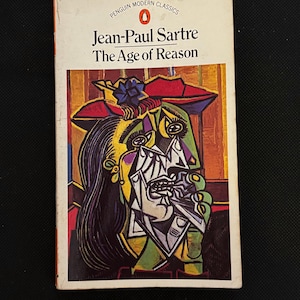 Może przedstawiać: Książka w miękkiej okładce zatytułowana "The Age of Reason" autorstwa Jeana-Paula Sartre'a. Okładka przedstawia kolorowy, abstrakcyjny portret w odcieniach zieleni, żółci, czerwieni i czerni. Książka należy do serii Penguin Modern Classics.
