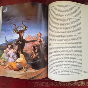 May include: An open book with a detailed illustration depicting a goat-like figure with horns surrounded by people in a historical setting. The page also contains printed text.