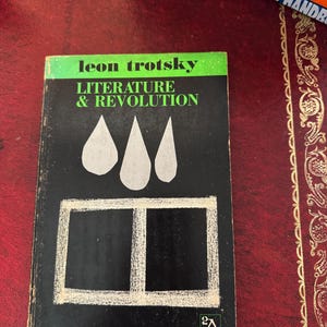 May include: A vintage paperback book titled "Literature & Revolution" by Leon Trotsky. The cover is black with white geometric shapes and green text. The book is part of the Ann Arbor Paperbacks series.