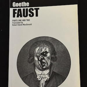 May include: A book cover for "Faust" by Goethe. The cover features a black and white portrait of a man in a circle, with the title and author's name in bold white text against a black background. The book is part of the "absolute classics" series.