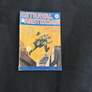 May include: Vintage comic book titled "Betrayal in Amsterdam." The cover features a dynamic illustration of a soldier leaping across rooftops, set against a yellow and orange sky. The comic is part of the Combat Picture Library series.