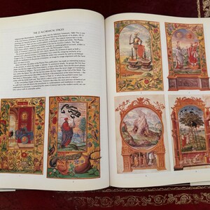 May include: Open book with colorful illustrations from "The 12 Alchemical Stages." The images are framed with ornate borders and depict figures and scenes in a medieval style. Text is visible on the pages.